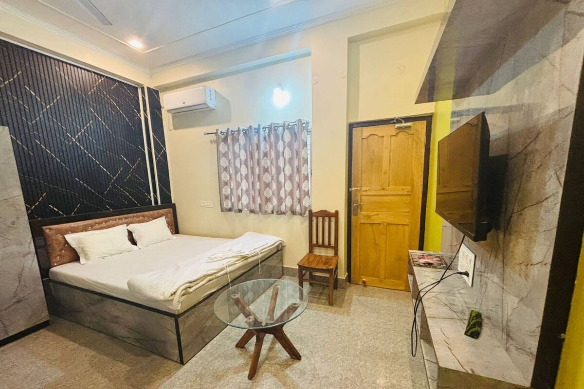 A bedroom with a bed, a glass table, a chair, a television, and a door.