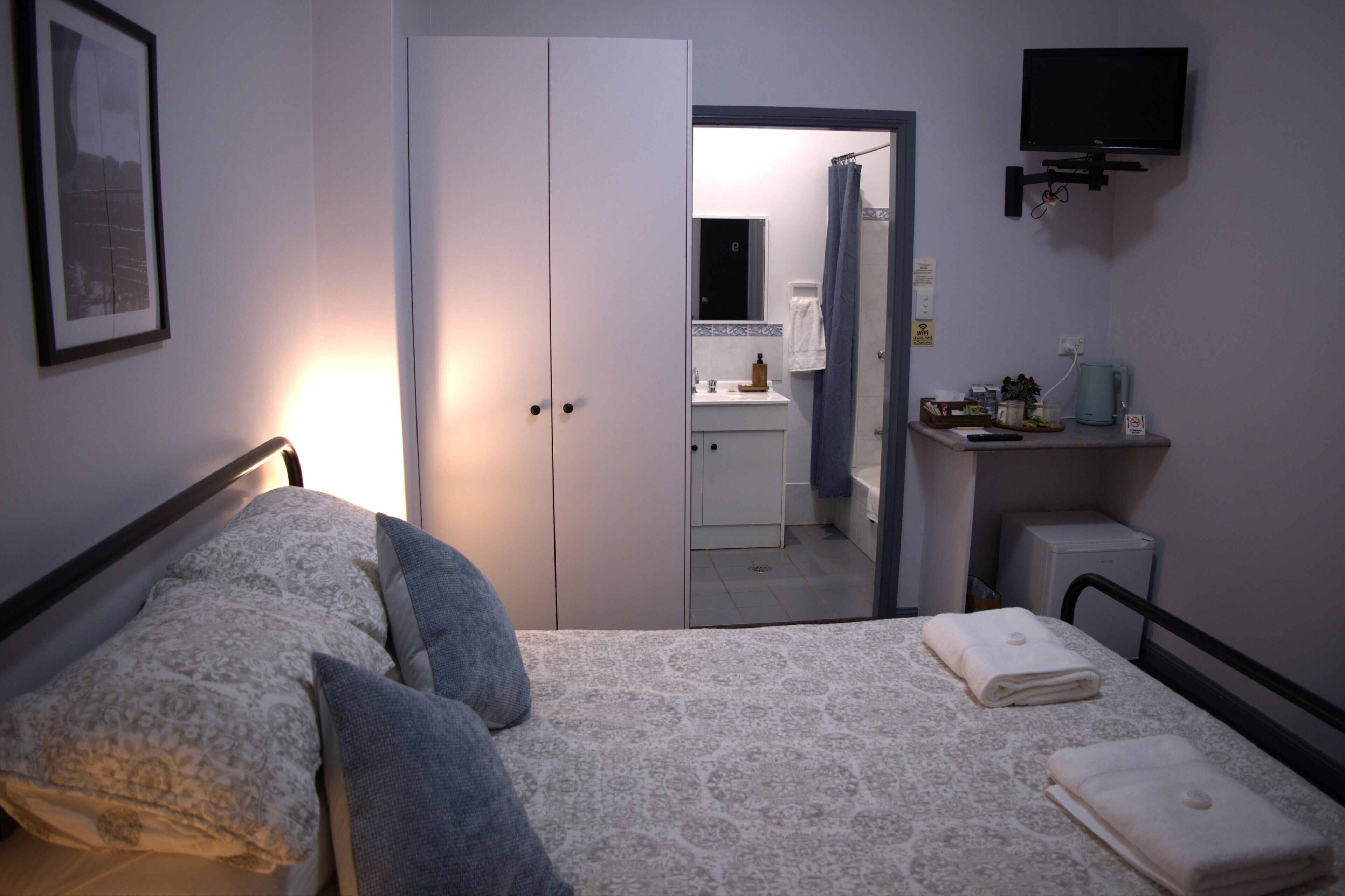 A bedroom with a bed, pillows, a TV, a bedside table, a mirror, and a bathroom visible through an open door.