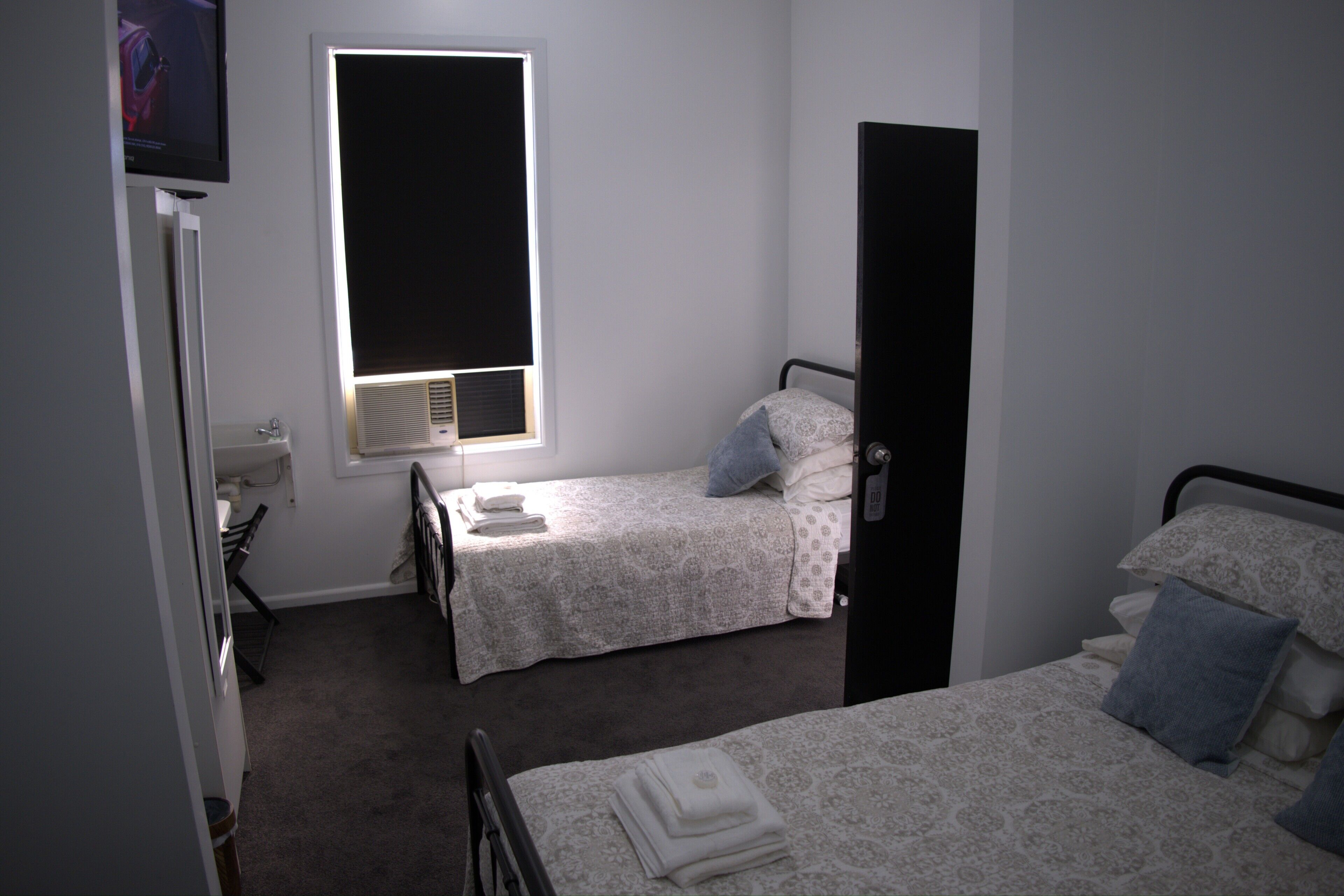 A bedroom with two beds, a window with blinds, a radiator, and a television on a stand.