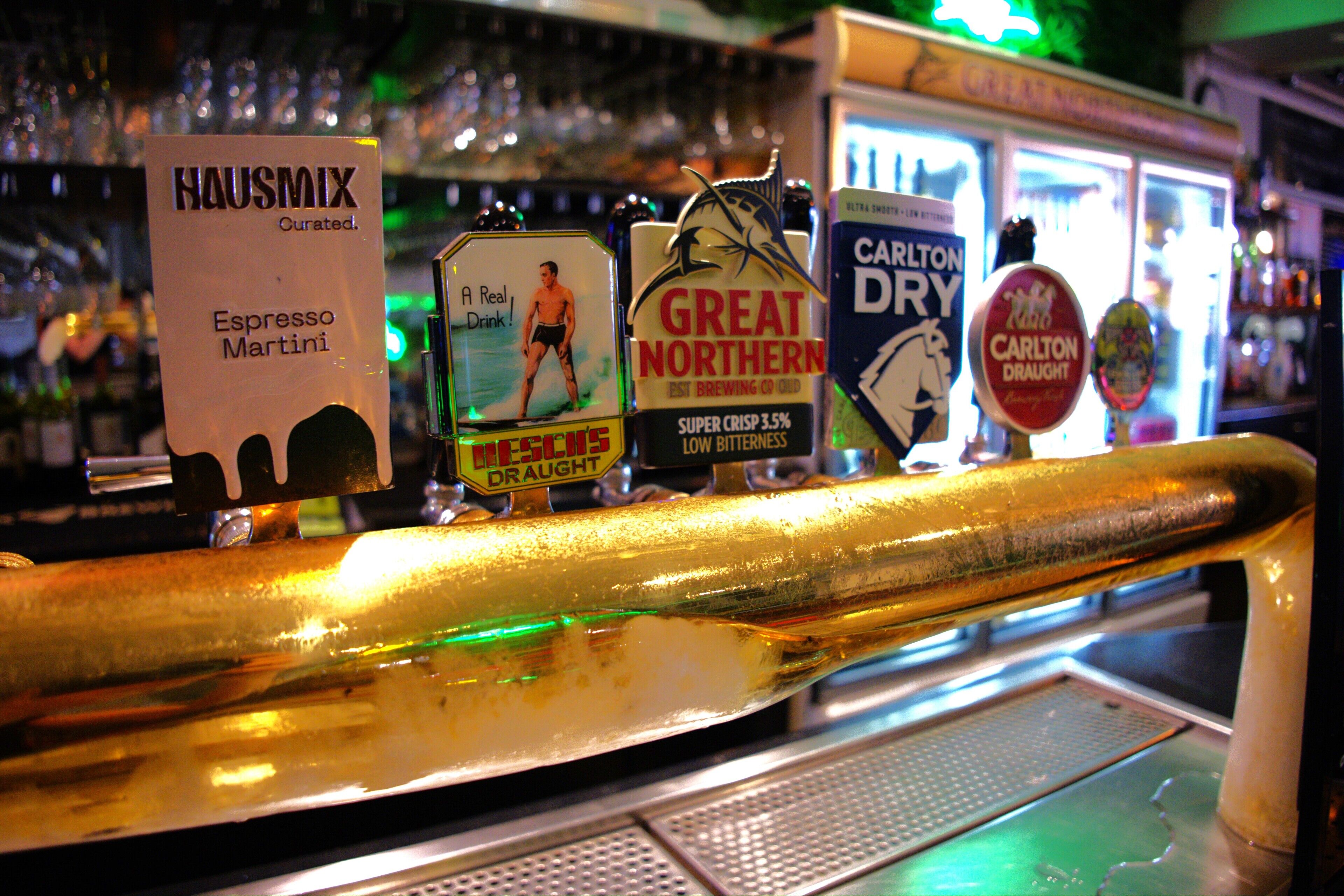 Um bar com diversas torneiras de cerveja, incluindo HAUSMIX, GREAT NORTHERN e CARLTON DRY.