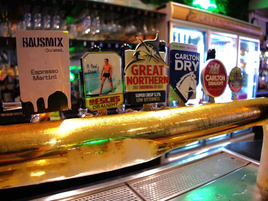 Um bar com diversas torneiras de cerveja, incluindo HAUSMIX, GREAT NORTHERN e CARLTON DRY.