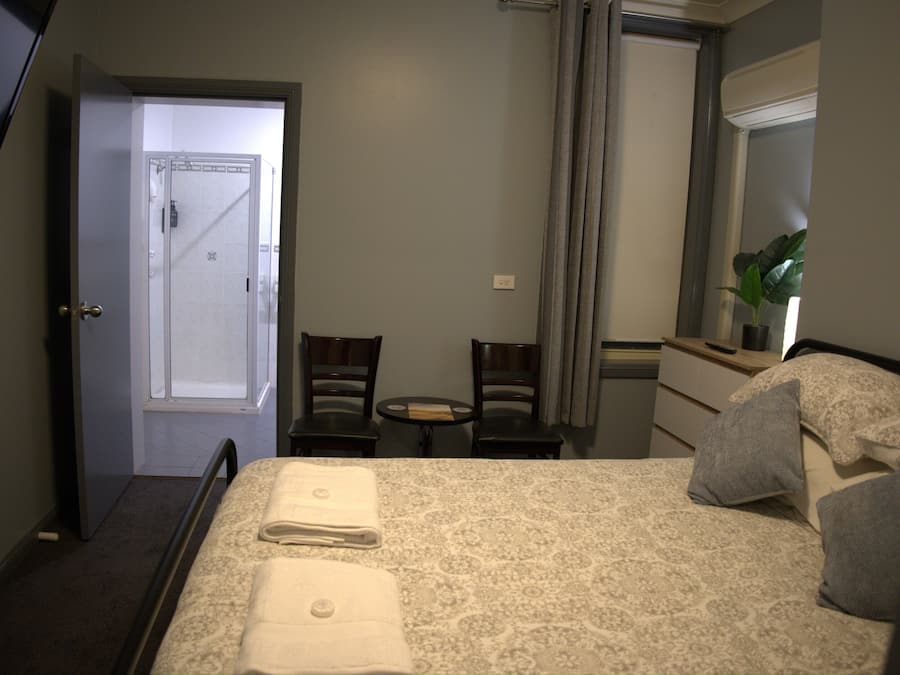 A hotel room with a bed, two chairs, a small table, a dresser, a mirror, and a door.