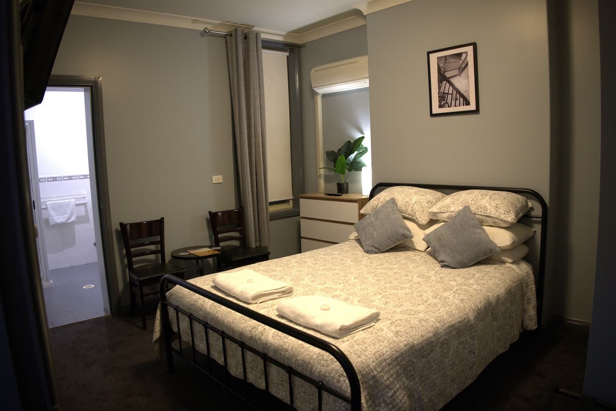 A bedroom with a bed, a chair, a desk, a mirror, and a window.