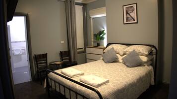Quarto com cama, cadeira, escrivaninha, espelho e janela.