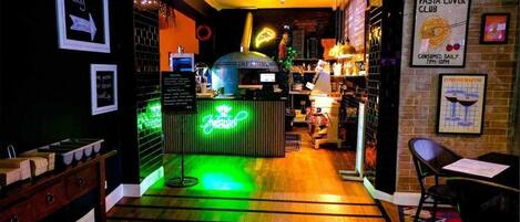 A restaurant interior with a neon sign, a pizza oven, and a menu board.