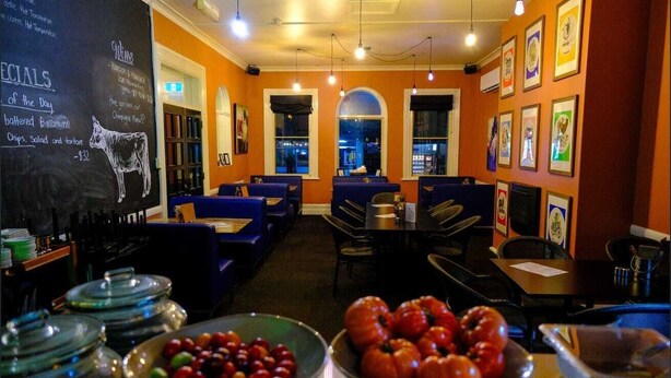 A restaurant with blue booths, a chalkboard menu, and a view of the city through arched windows. - The Imperial Hotel (Cowra)