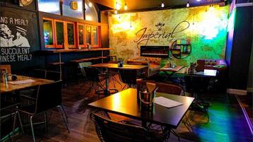 A restaurant with tables and chairs, a brick wall, and a neon sign.