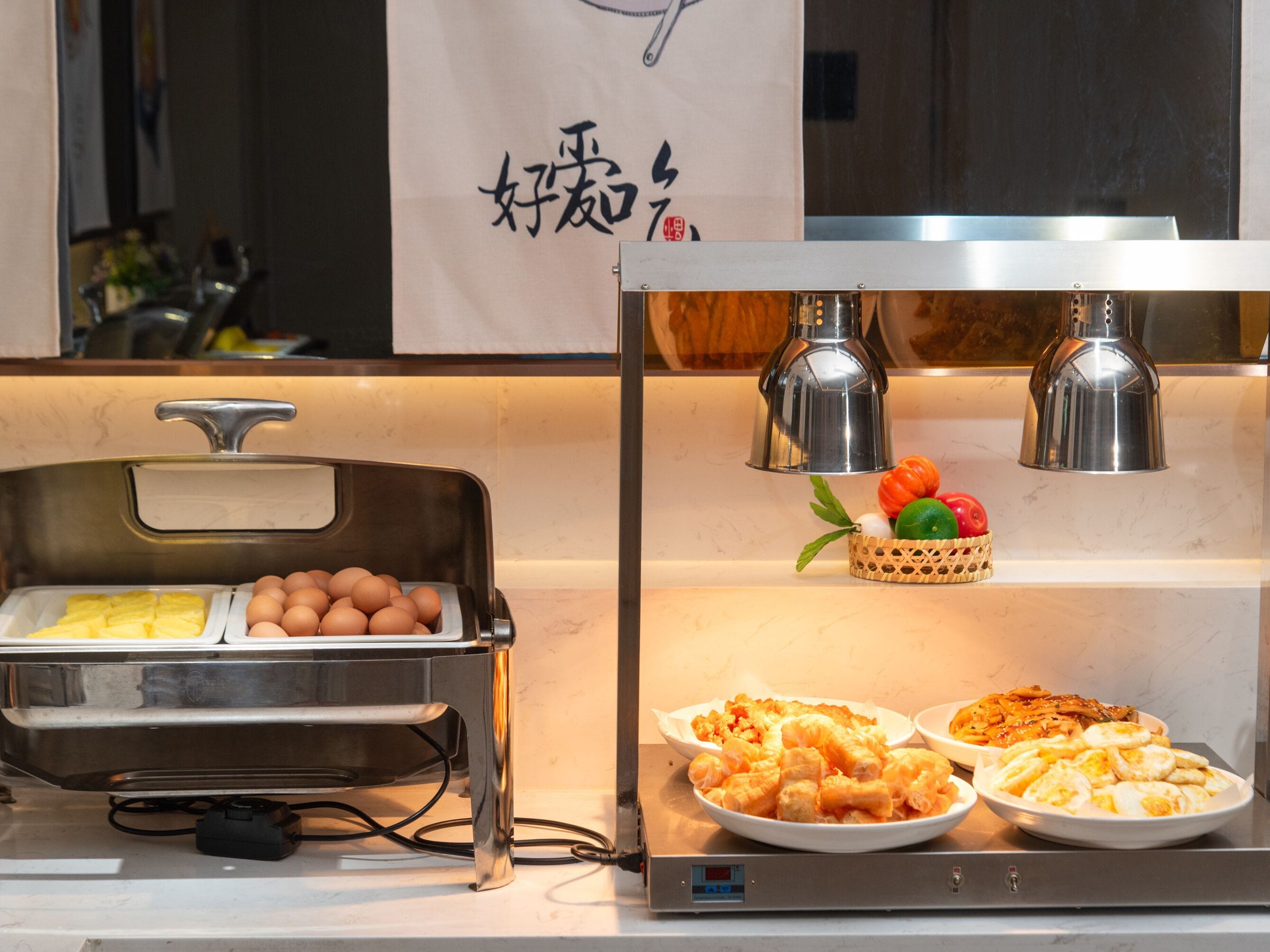Disposição de buffet com diversos alimentos, um visor digital e uma parede decorativa com uma placa pendurada.