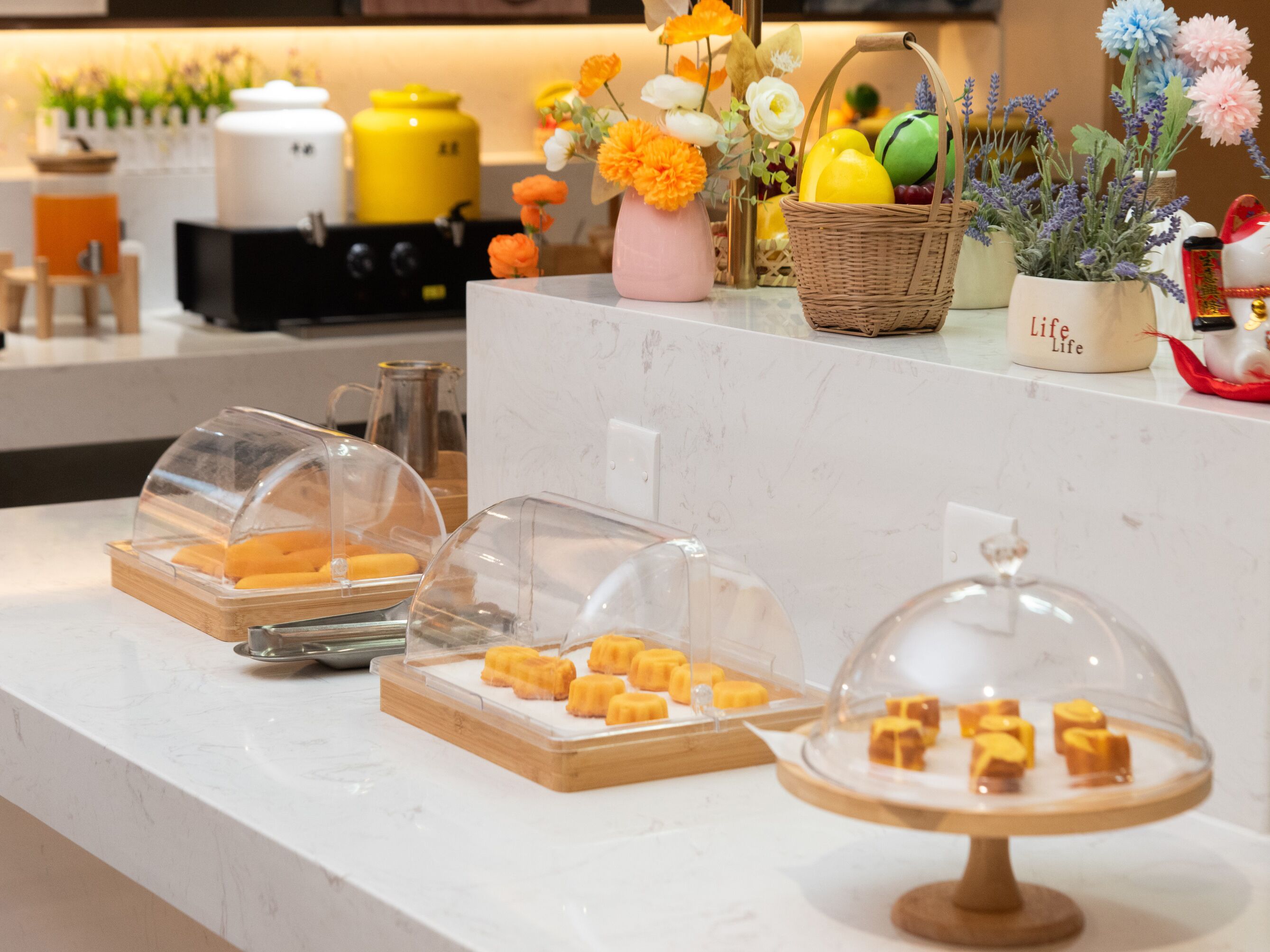 Una encimera de cocina con alimentos cubiertos, una cesta de frutas y flores decorativas.