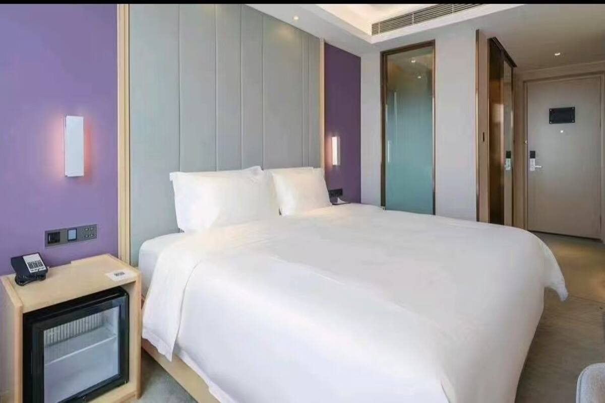 Una habitación de hotel moderna con una cama grande, un escritorio, una silla y un mini bar.