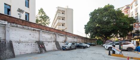 A parking lot with multiple cars, a white building with a red roof, and a tree in the background.