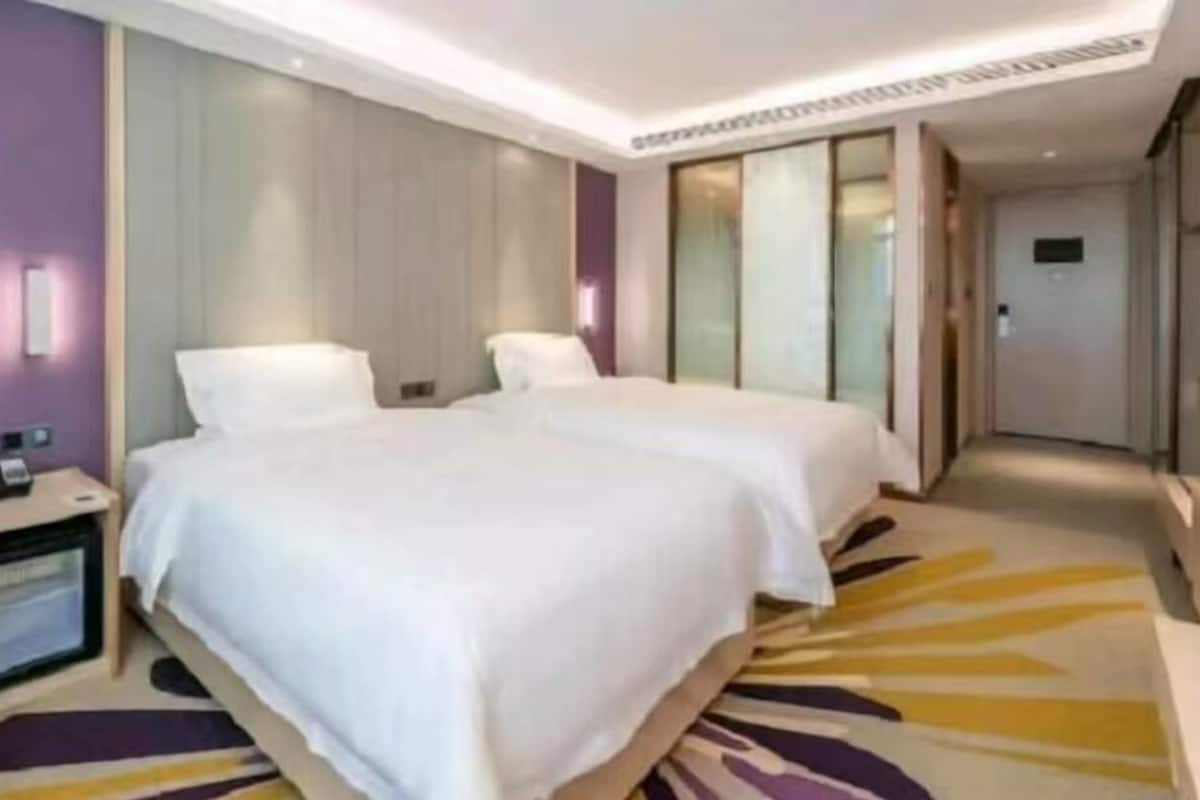 Habitación de hotel con dos camas, una mesita de noche con lámpara, un televisor de pantalla plana y un ventanal grande.