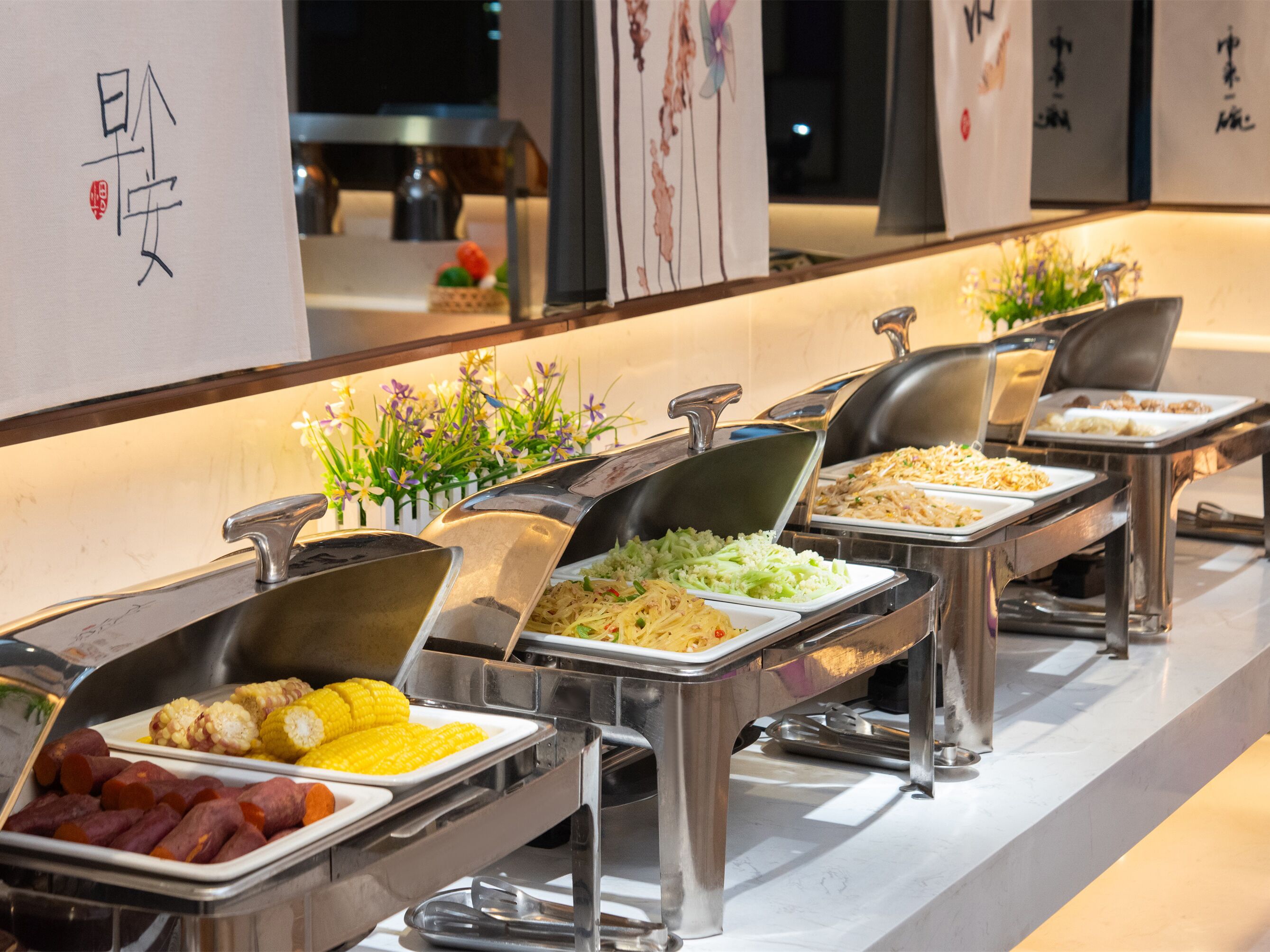 A buffet with various food options, including corn, sweet potatoes, and rice dishes.