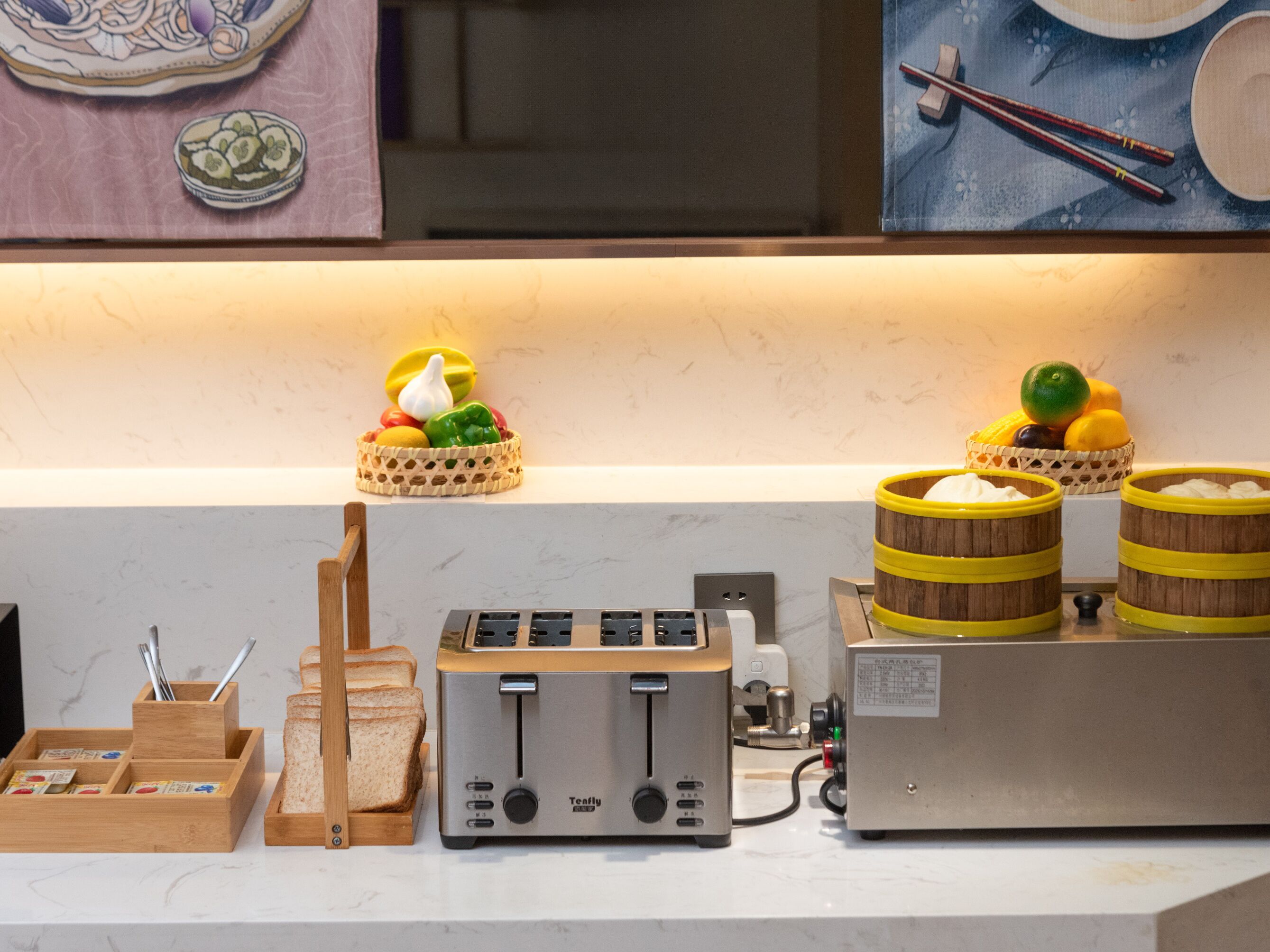 A kitchen counter with a toaster, a bread rack, a fruit basket, and two wooden containers.