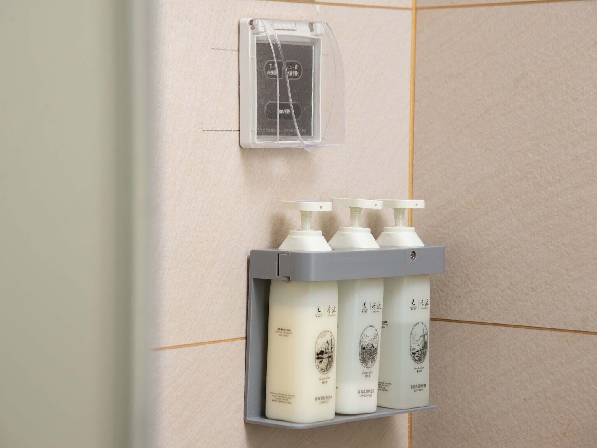 A bathroom with a shelf holding four bottles of shampoo and conditioner.