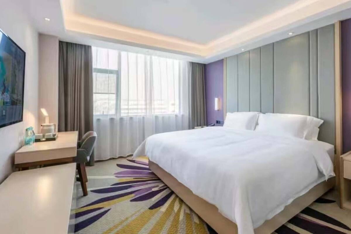 Habitación de hotel con una cama grande, un escritorio, una silla, un televisor y una ventana con cortinas.