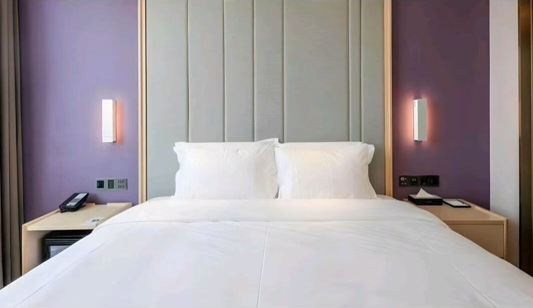 A hotel room with a large bed, two bedside tables, a wall-mounted phone, and a light fixture on the wall.