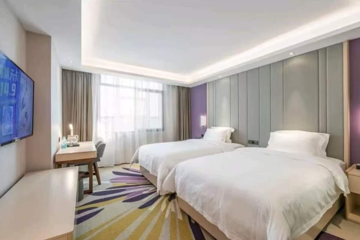 Habitación de hotel con dos camas, un escritorio, un televisor y un ventanal amplio.