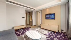 Una habitación de hotel con sofá, una pequeña mesa redonda, un armario, televisión montada en la pared y una alfombra estampada.