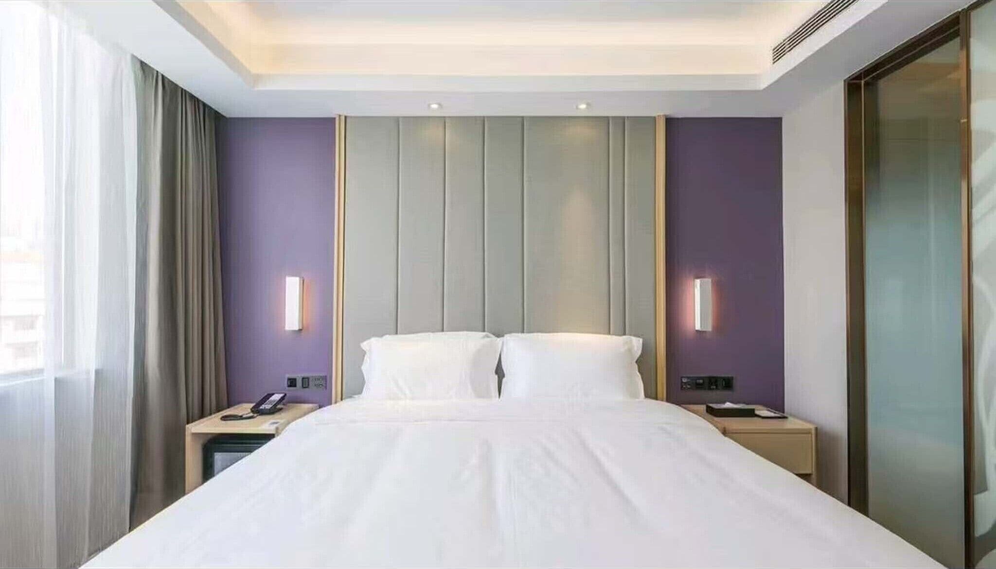 Een hotelkamer met een bed, twee nachtkastjes, een telefoon en een wandlamp.