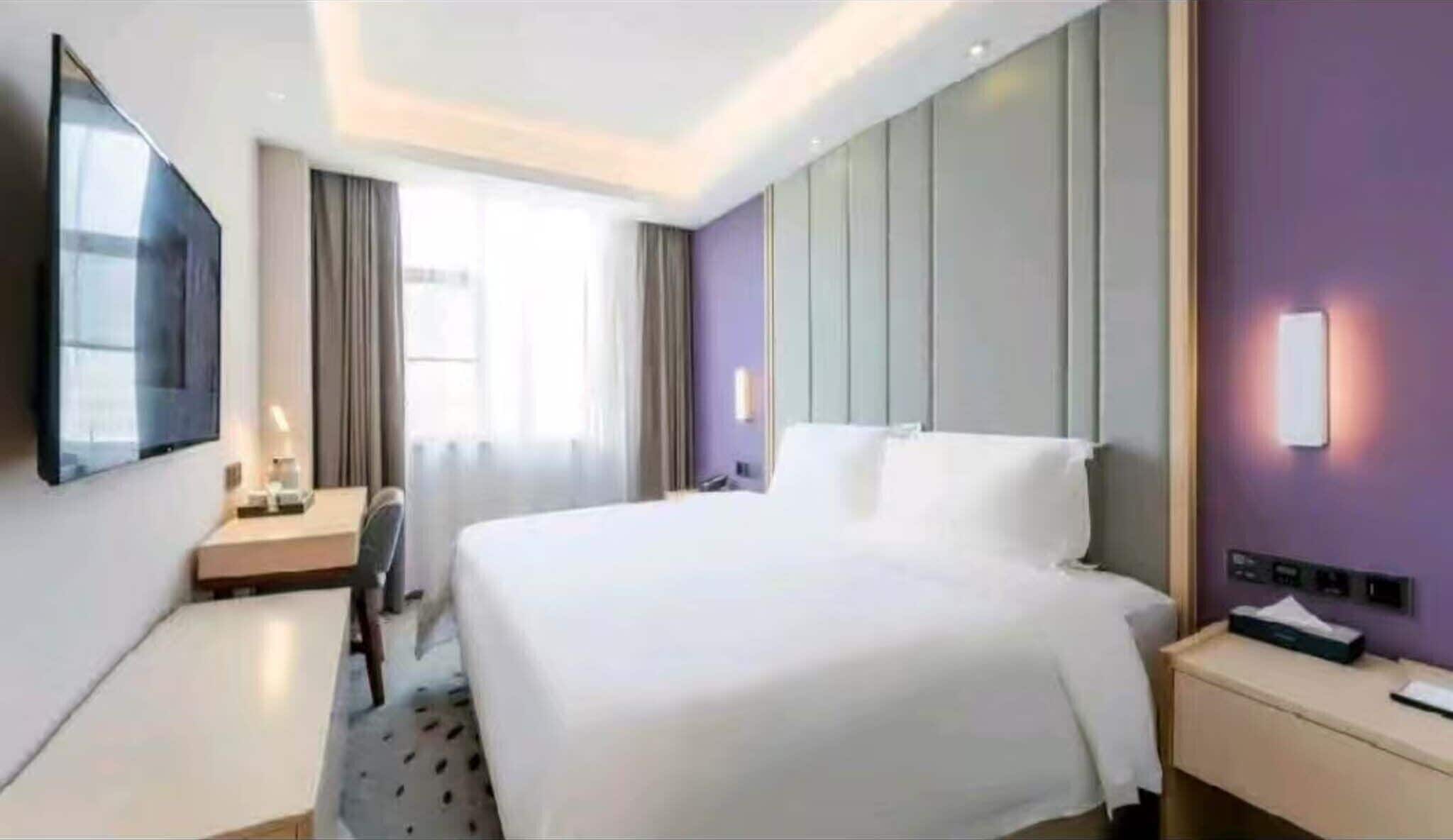 A hotel room with a bed, a desk, a chair, a TV, and a window with curtains.