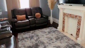 Una sala de estar con un sofá, televisión, chimenea y un ventanal con cortinas.