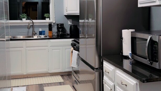 Una cocina moderna con gabinetes blancos, electrodomésticos de acero inoxidable y piso de madera.
