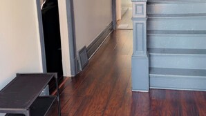 Un pasillo con suelo de madera, una escalera y una puerta que da a otra habitación.