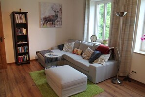 Ein Wohnzimmer mit Sofa, Hocker, Bücherregal und Kunstwerken.