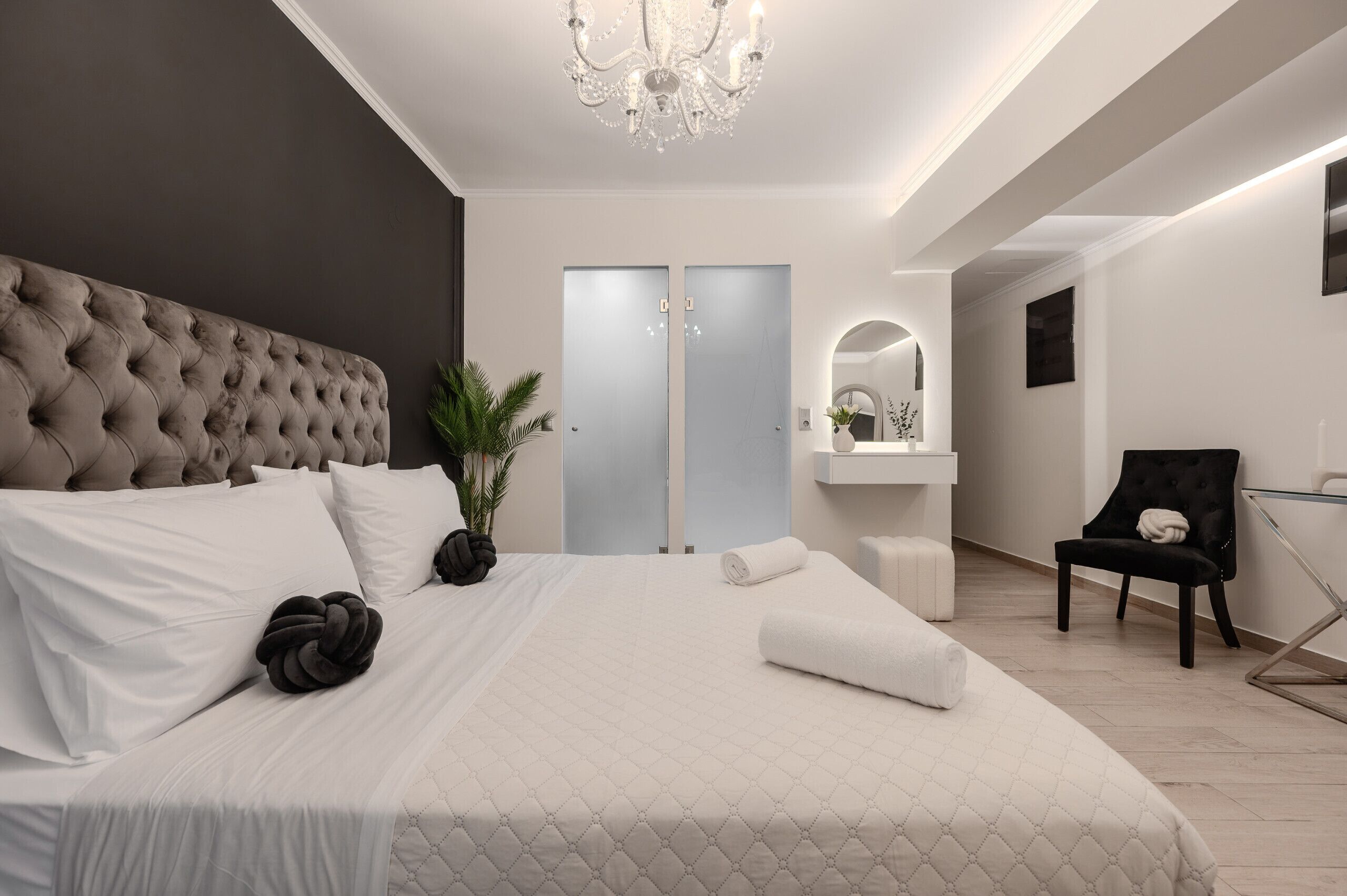 A modern bedroom with a tufted headboard, a large bed, a potted plant, a chair, and a mirror.