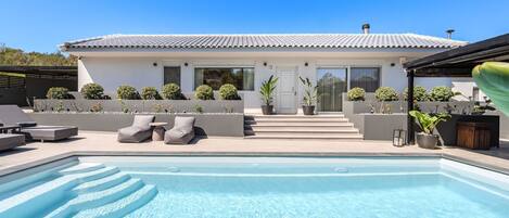 A modern house with a swimming pool, outdoor seating, and potted plants.