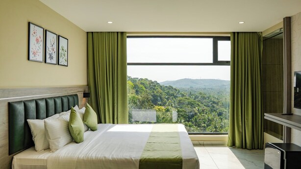 Une chambre d’hôtel avec un lit, des rideaux verts, une télévision et une vue sur une forêt.