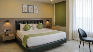 Une chambre d’hôtel comprenant un lit, des tables de chevet, une chaise, une fenêtre avec des rideaux et des œuvres d’art accrochées au mur.