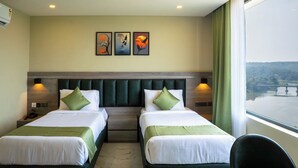 Une chambre d’hôtel avec deux lits, une tête de lit, des lampes de chevet, une table de chevet, une chaise et une fenêtre donnant sur un paysage agréable.