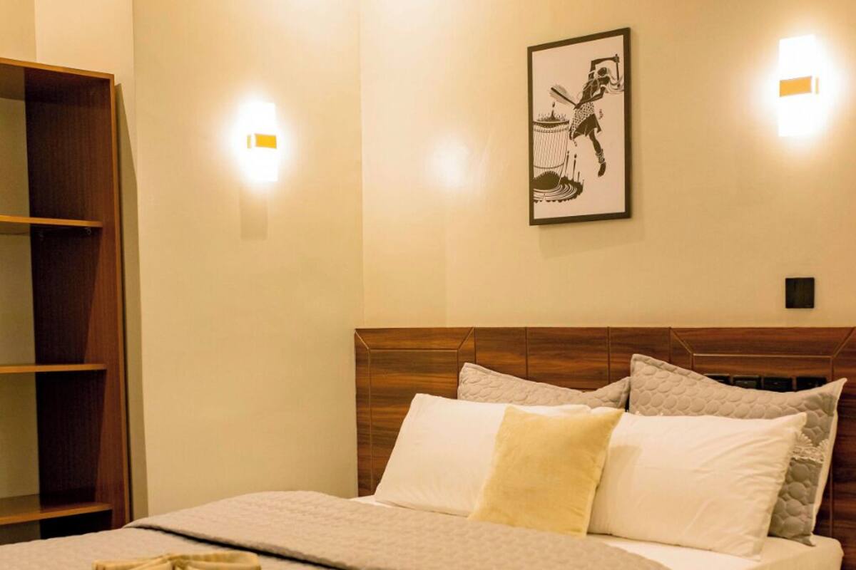 Un lit bien fait, avec une tête de lit en bois, une table de chevet et un luminaire fixé au mur.