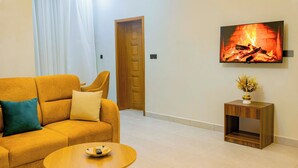 Una sala de estar con un sofá, una mesita, un televisor montado en la pared y una puerta al fondo.