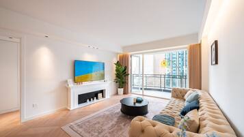 Een moderne woonkamer met een bank, een open haard, een televisie en een balkon met uitzicht over de stad.