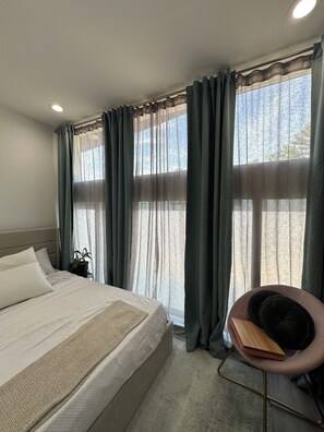 A bedroom with a bed, a chair, a potted plant, and large windows with curtains. - Serene 1-bedroom townhome with AC near ATL Airport (College Park)