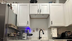 Una cocina moderna con armarios blancos, un refrigerador de acero inoxidable, un lavavajillas y una cafetera.