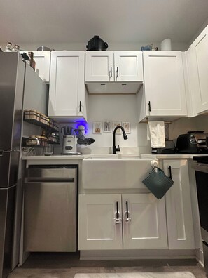 A modern kitchen with white cabinets, a stainless steel refrigerator, a dishwasher, and a coffee maker. - Serene 1-bedroom townhome with AC near ATL Airport (College Park)