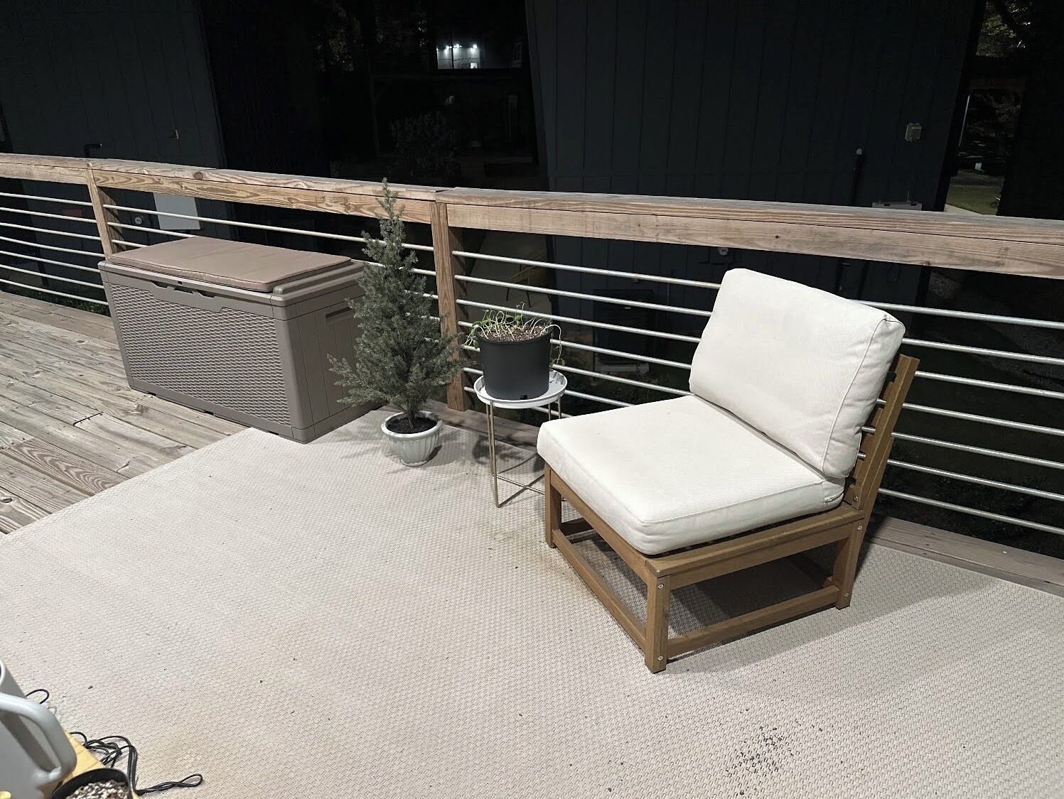 Ein Balkon mit einem Holzstuhl, einem kleinen Tisch, einem Topfpflanzen und einem Korbwäsche.