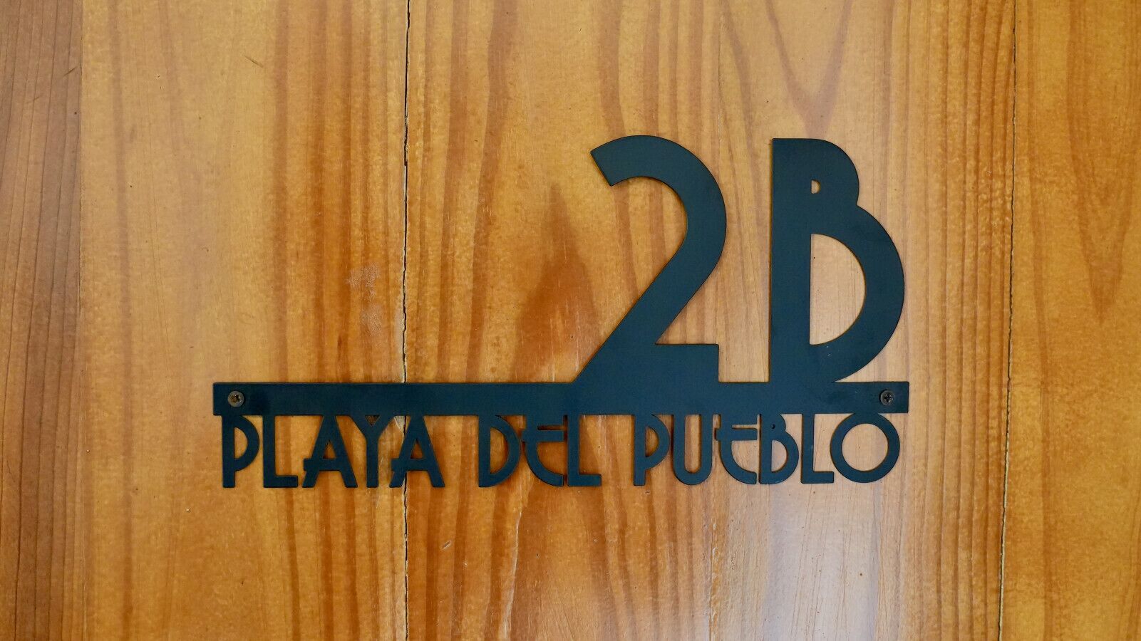 Una puerta de madera con un letrero de metal que dice "2B Playa del Pueblo".