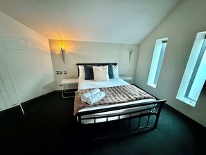 Een moderne hotelkamer met een bed, nachtkastje, wandlamp en een raam.