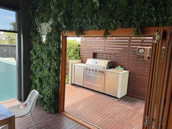 Une cuisine extérieure équipée d’un barbecue, d’une terrasse en bois et d’une chaise.