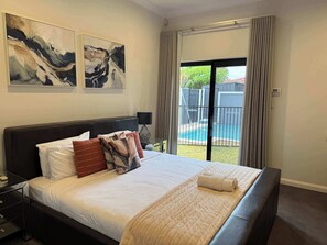 Une chambre d’hôtel avec un lit, une table de chevet, une lampe et une vue sur une piscine.