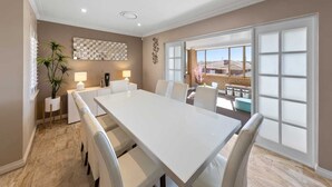 A spacious dining area with a long white table, comfortable chairs, and a view of the outdoors through large windows. - 47 Ultimate Entertainer! Pool, Man Cave, Kids Play (Stirling)