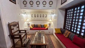 Una sala de estar con sofá, una silla de madera, una mesa de centro, relojes en la pared y un panel decorativo.