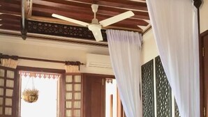 Un dormitorio con cama, ventilador de techo, ventana con cortinas y un panel decorativo en la pared.
