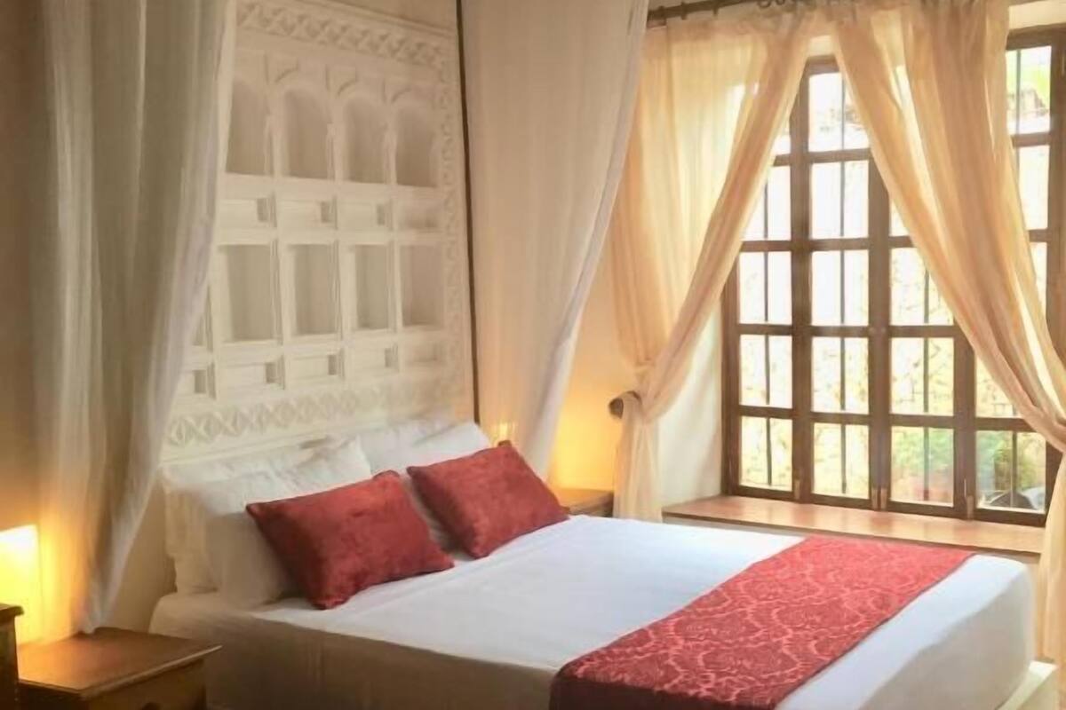 A bed with a canopy, a nightstand, and a window with curtains.