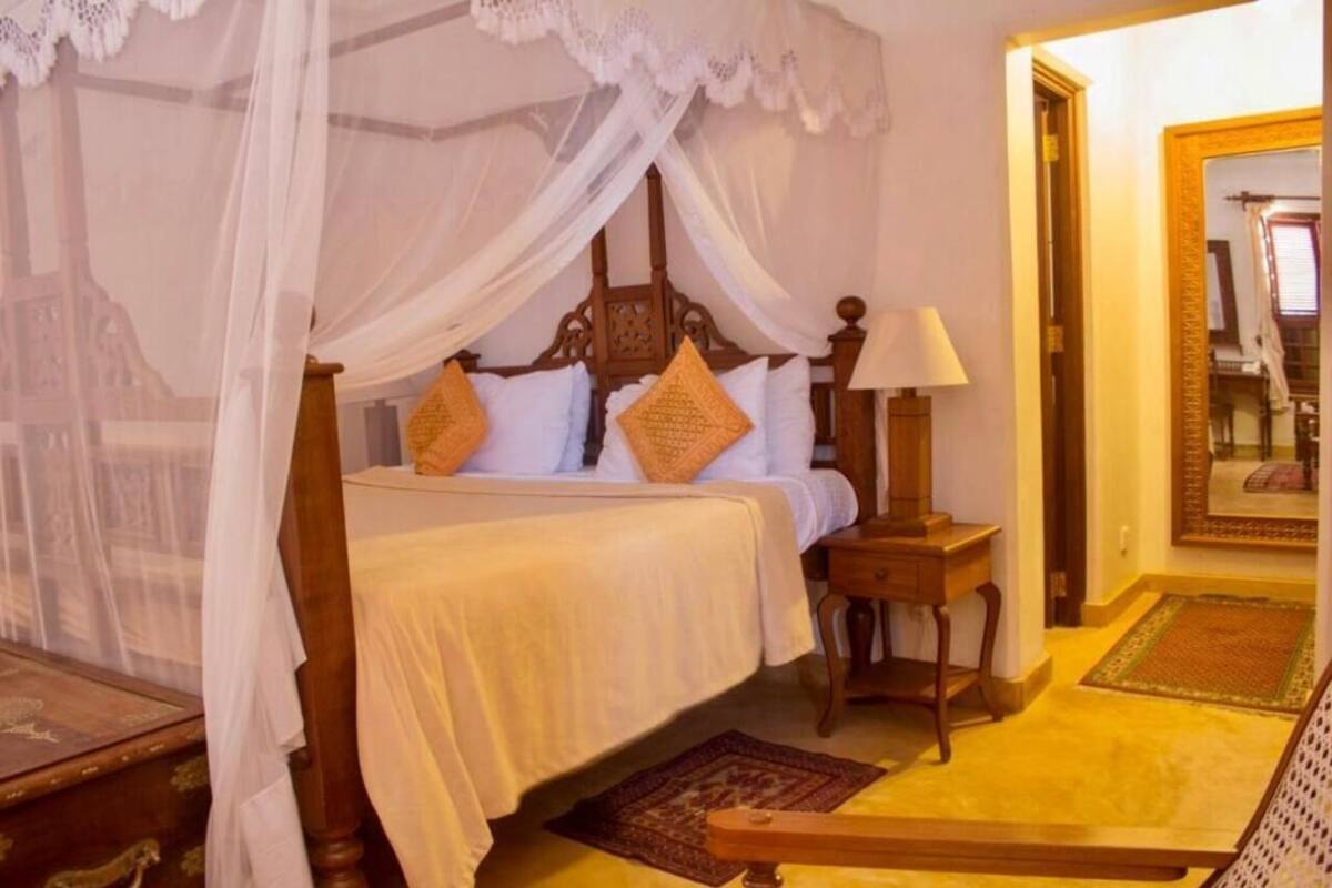 A bed with a canopy, a nightstand, a lamp, and a mirror.